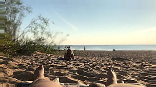 Un exhibicionista público muestra su pene en una playa desnuda antes de correrse.